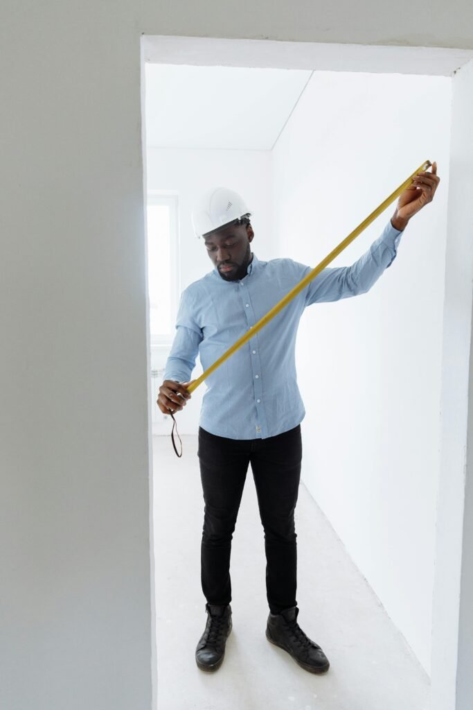pexels-photo-8470780-8470780 Adult male construction worker measuring room dimensions with a tape measure.
